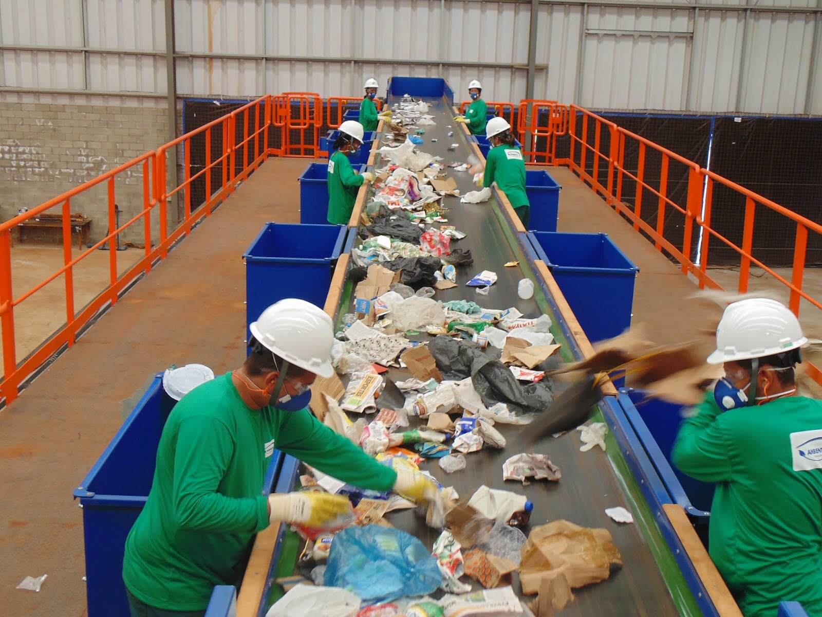 trabalhadores de uma fábrica de resíduos separando lixo em uma esteira 