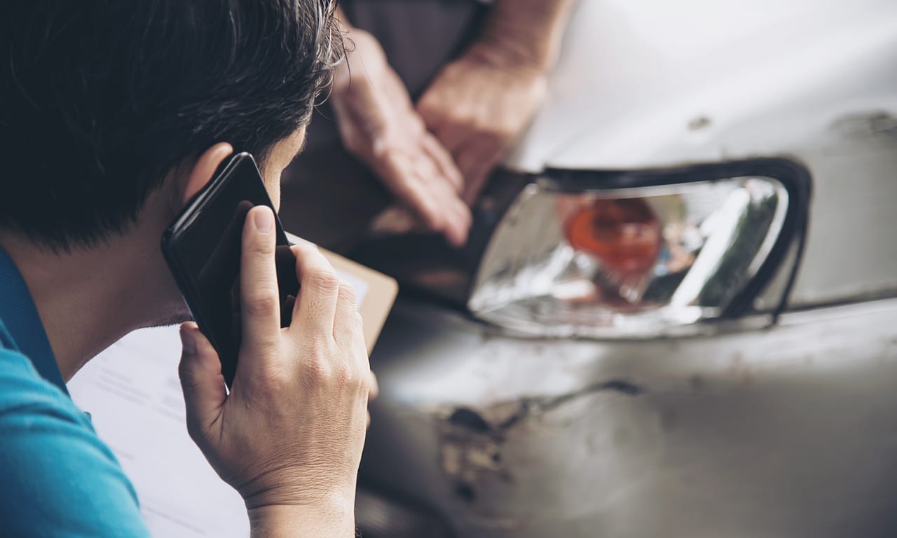 motorista falando ao celular com o carro sinistrado a sua frente