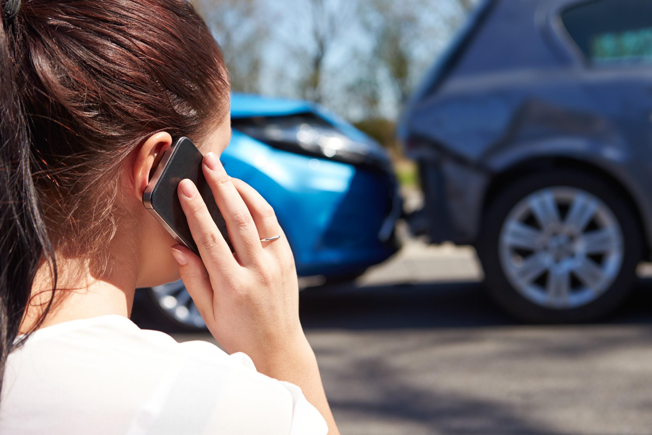 mulher falando ao celular enquanto dois carros aparecem colididos 