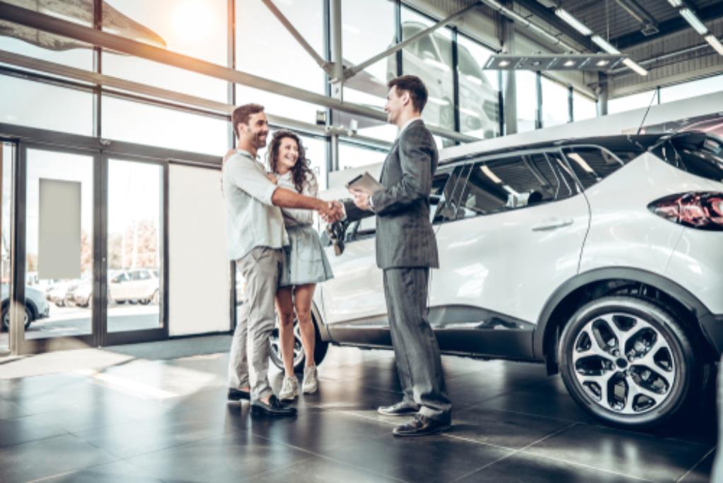 Casal comprando o seu carro seminovo em uma agência com um consultor, aproveitando os valores mais baixos dos produtos.